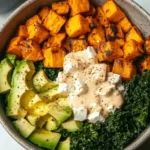 Bowl of roasted sweet potatoes, chicken, avocado, kale, feta, and dressing on rice, shot from above in high resolution