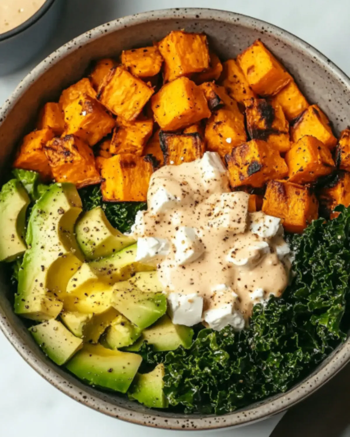 Bowl of roasted sweet potatoes, chicken, avocado, kale, feta, and dressing on rice, shot from above in high resolution
