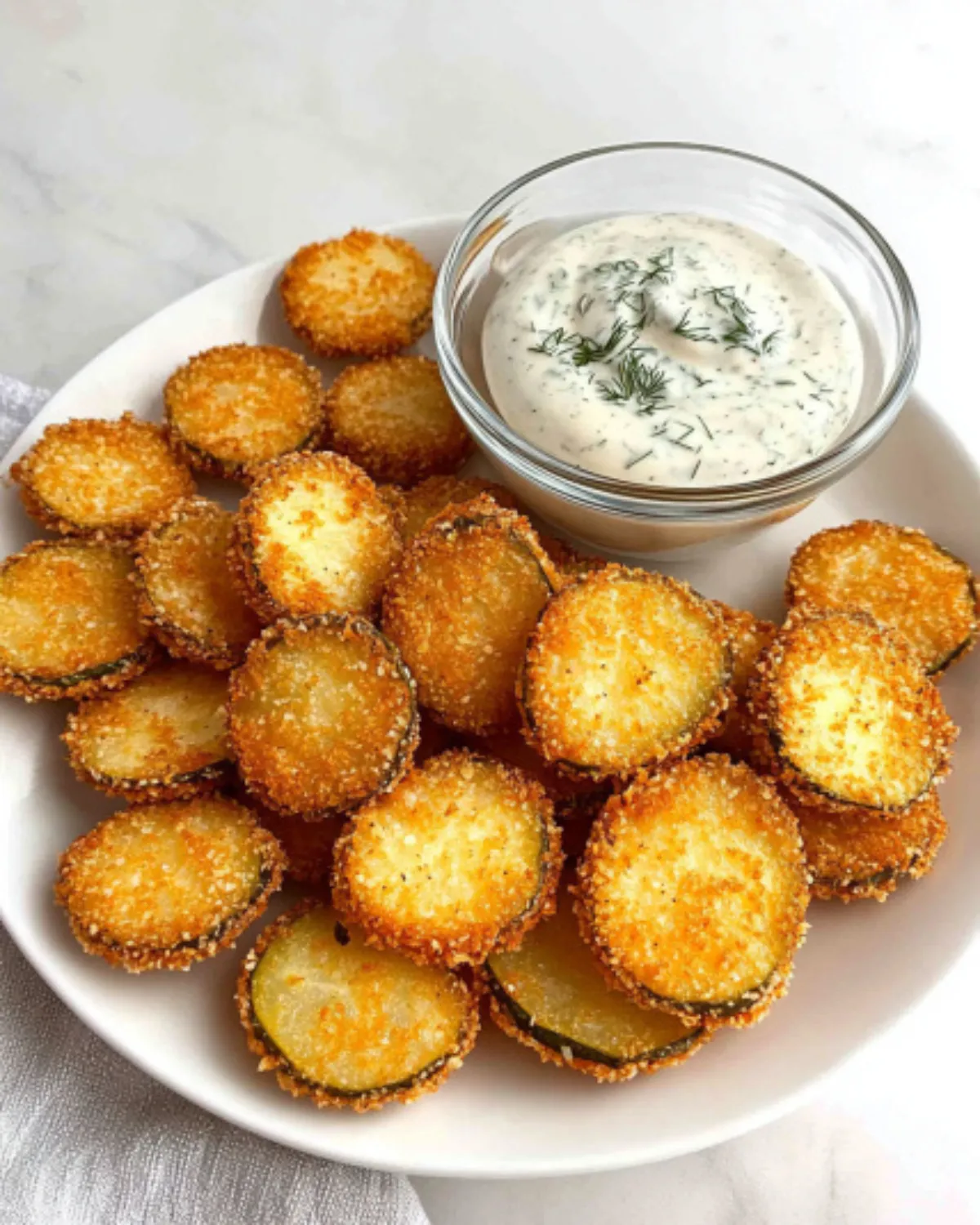 Crispy air fryer fried pickle chips with golden panko crust and creamy dill dip on a white plate