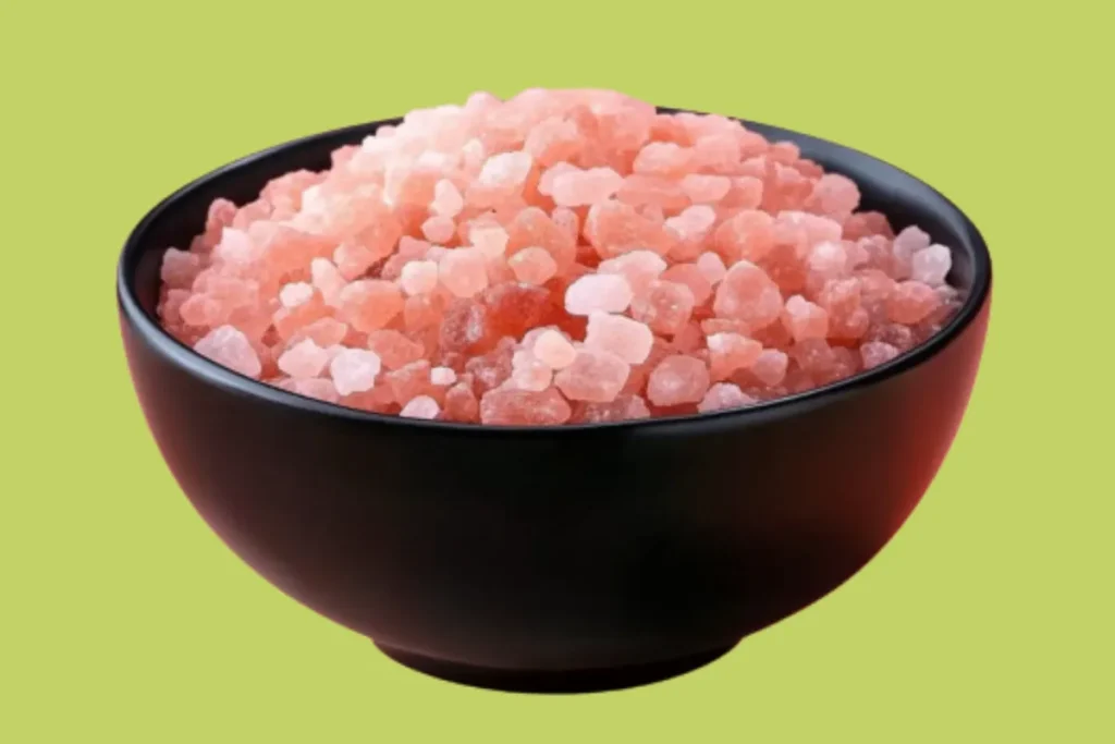 Close-up of a black bowl filled with Himalayan pink salt against a pastel pink background

