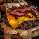 Close-up of a bacon cheeseburger with cheddar, crispy bacon, and peppered creamy sauce dripping over a grilled beef patty.