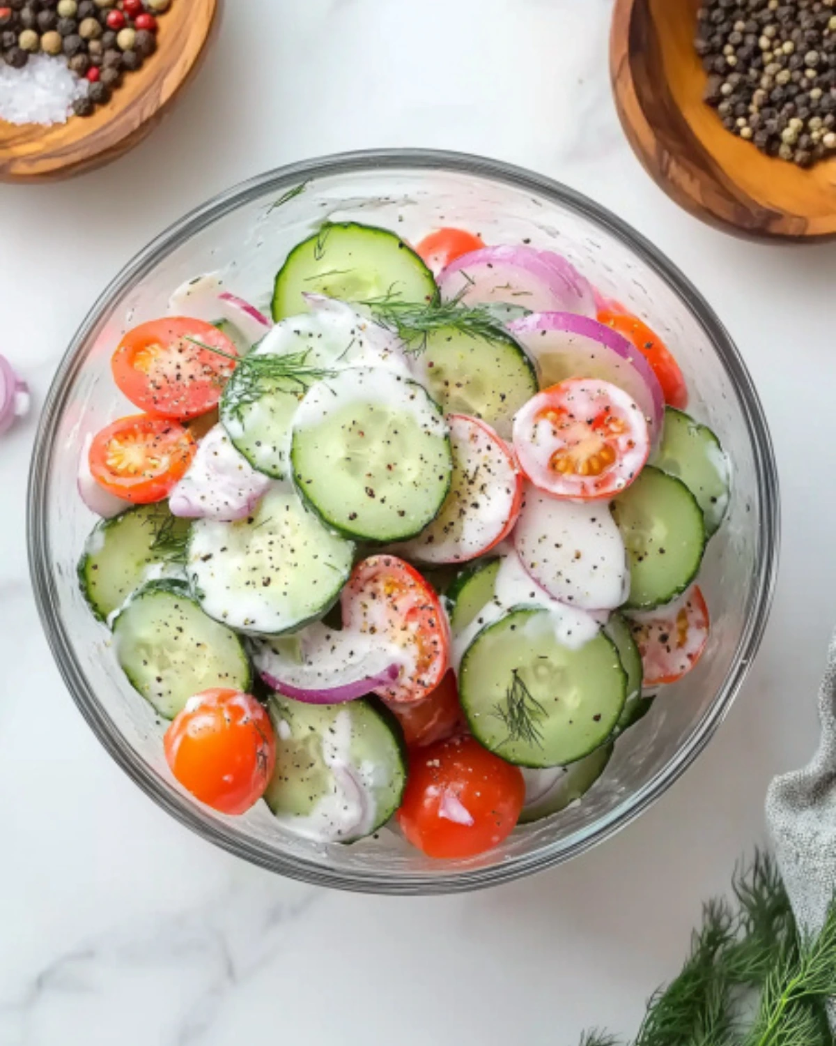 Top view of creamy cucumber tomato salad with dill, cherry tomatoes, and red onions in a glass bowl