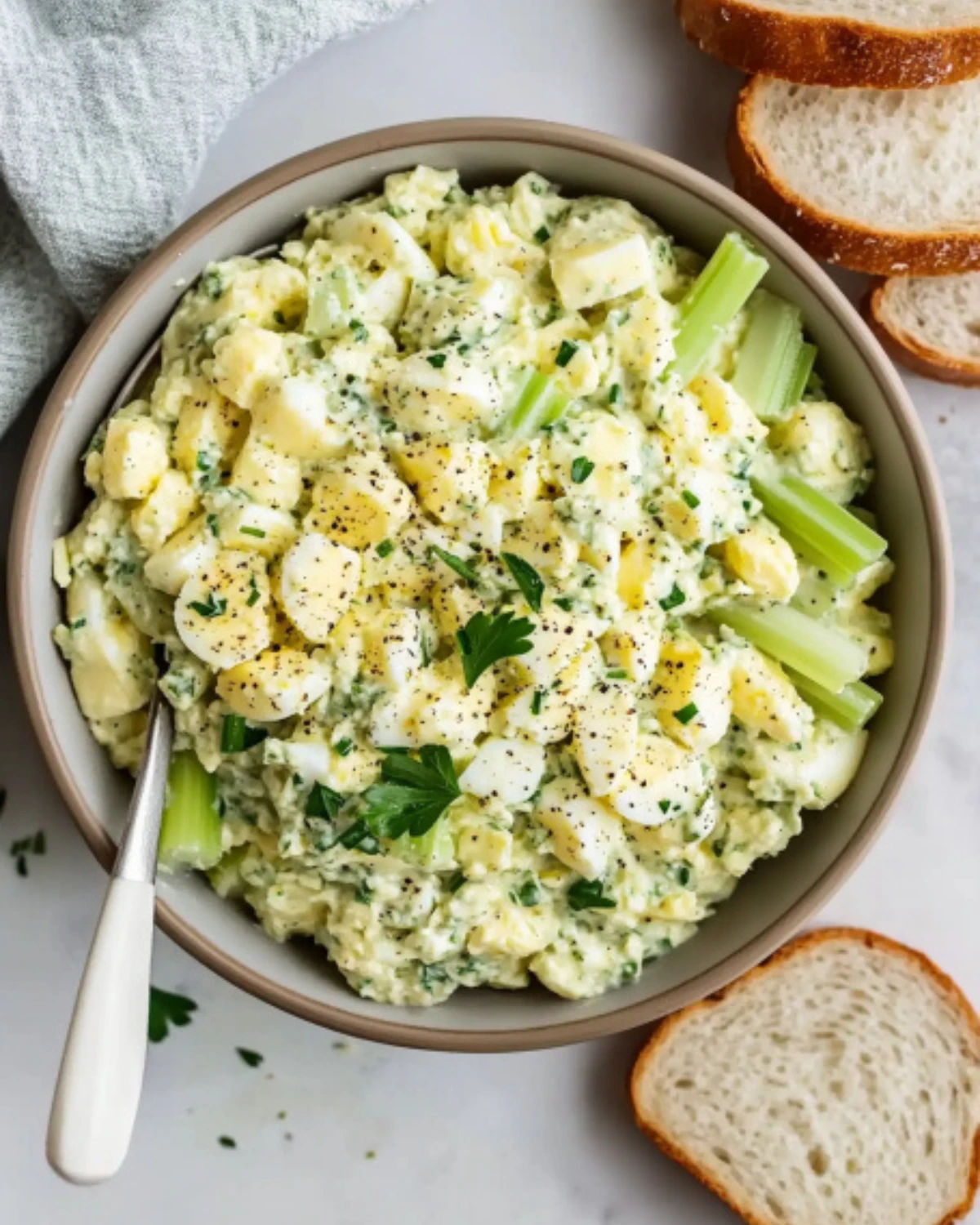 Bowl of healthy egg salad made with Greek yogurt, celery, and parsley served with sliced bread