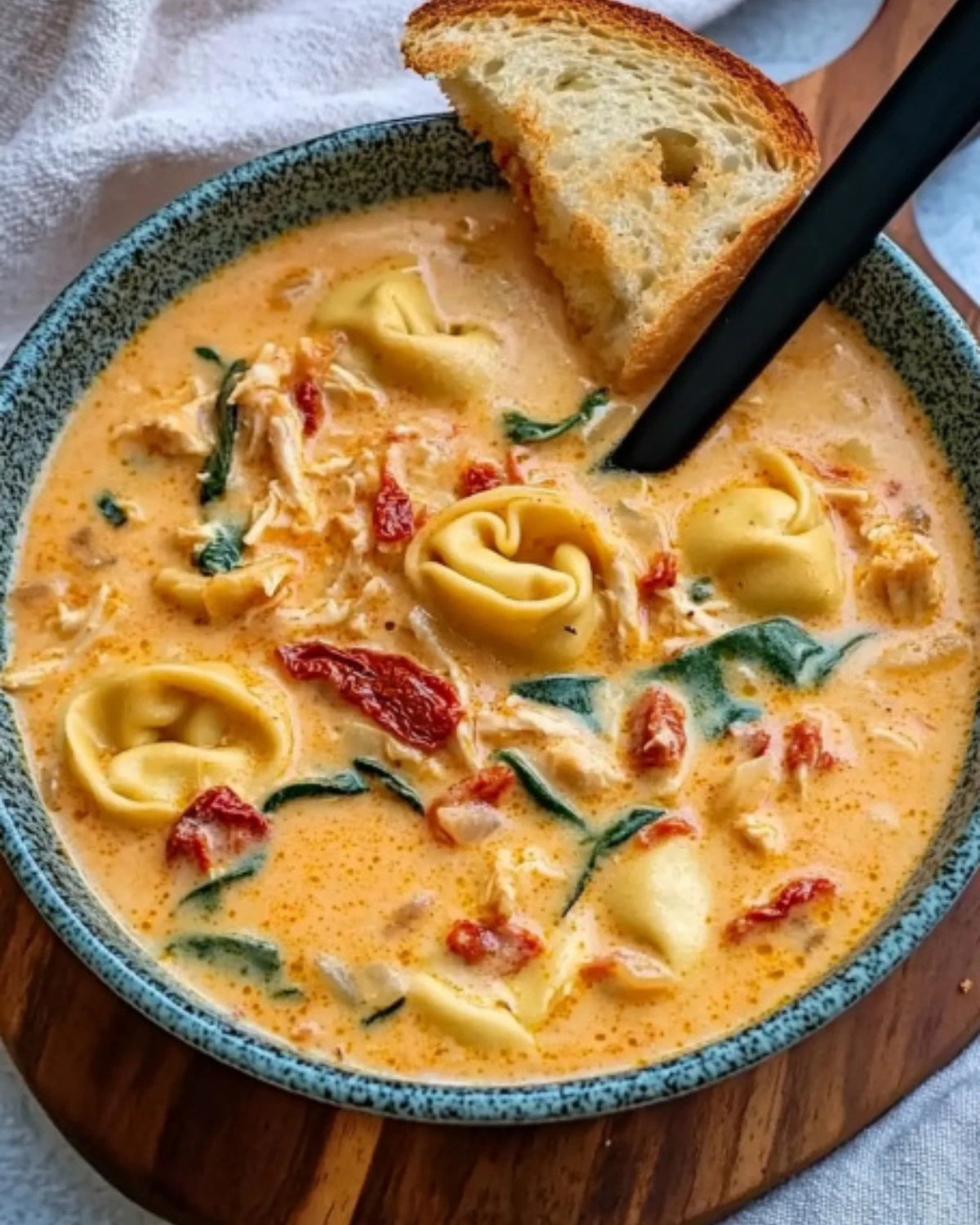 Bowl of Marry Me Chicken Soup with tortellini, spinach, sun-dried tomatoes, and toasted bread on a wooden board