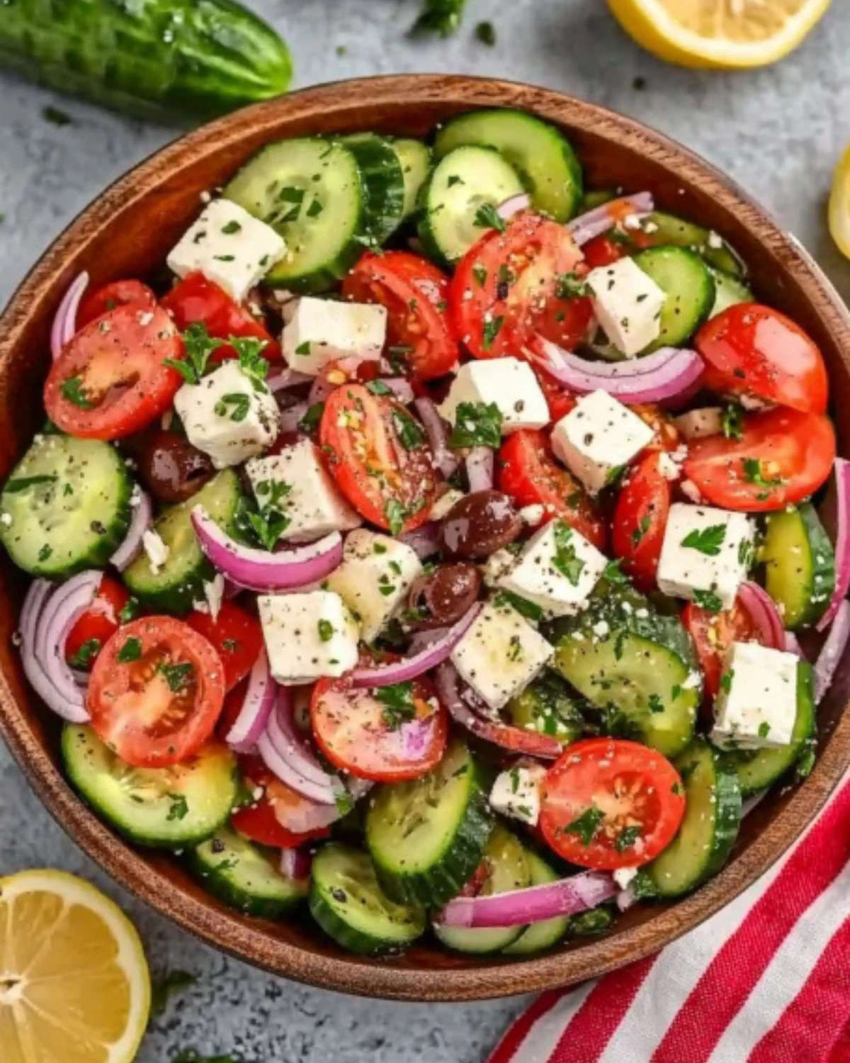 Top-down view of Mediterranean salad with cucumbers, cherry tomatoes, feta cheese cubes, kalamata olives, and red onion in a wooden bowl