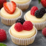 Mini cheesecakes topped with fresh strawberries, raspberries, and blackberries on a gray stone background