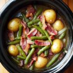 Slow cooker green beans, baby potatoes, and bacon in broth inside a black crockpot on wooden table