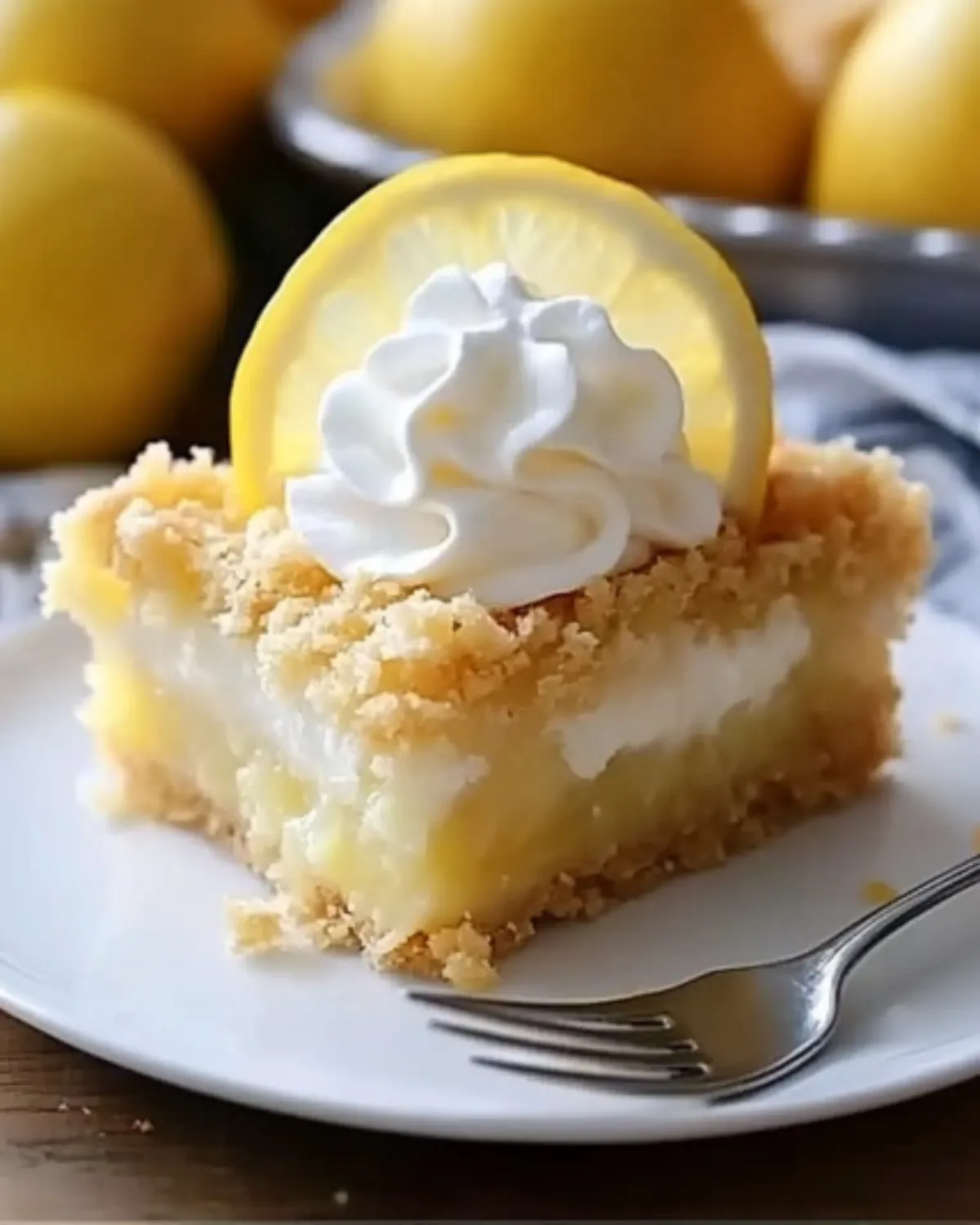 Close-up of a lemon cream cheese dump cake slice with whipped cream and lemon slice on a white plate with a fork.