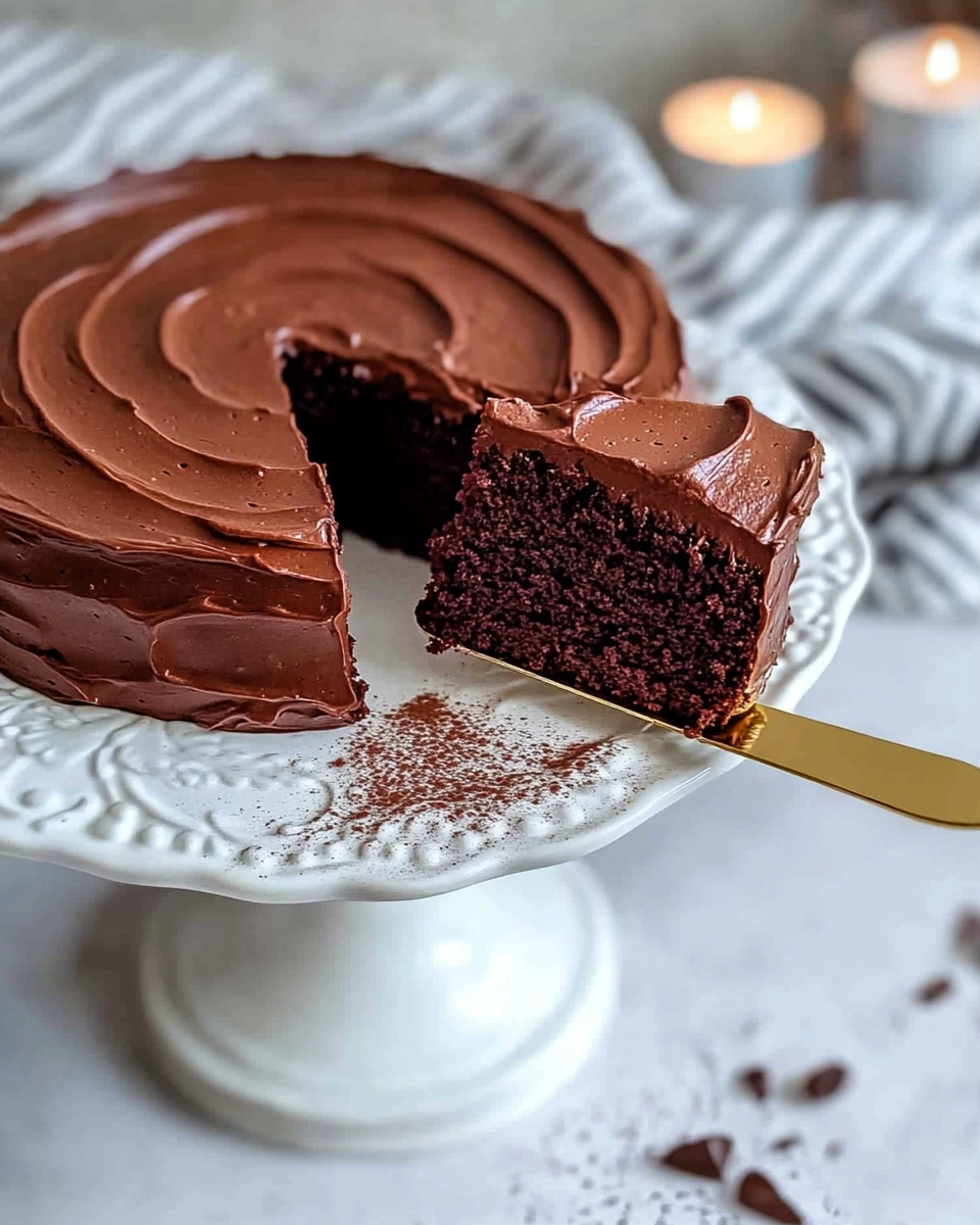 Moist chocolate cake with creamy frosting on a white floral cake stand, one slice lifted with golden cake server