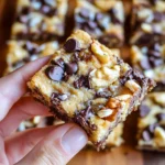 Hand holding a gooey magic cookie bar with chocolate chips, coconut, and walnuts.