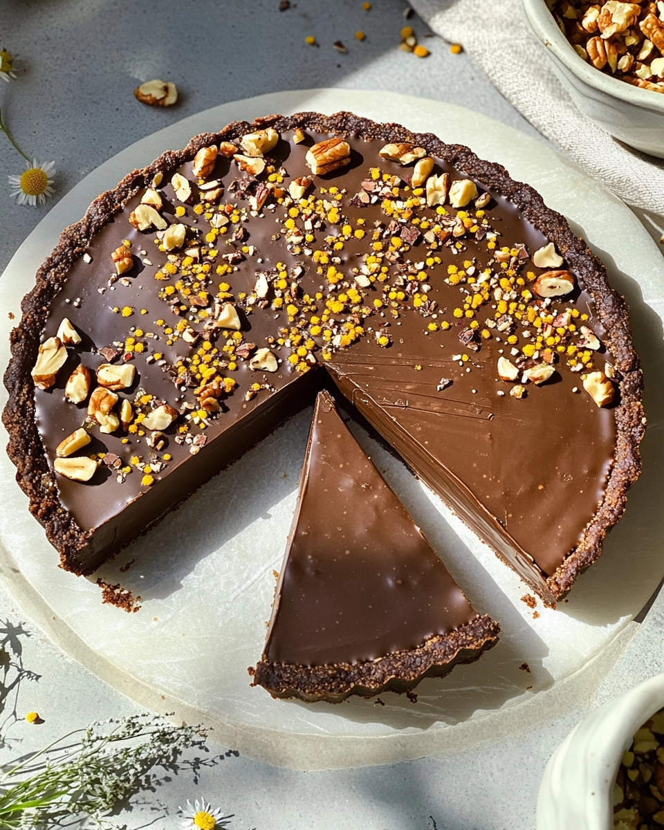 Overhead photo of a sliced raw vegan chocolate tart topped with nuts, cacao nibs, and bee pollen on a stone background in natural sunlight.