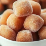 Golden sugar-coated dough balls piled in a white bowl, showcasing their crispy texture, perfect for dipping in chocolate sauce.