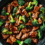 Close-up of beef and broccoli stir-fry over white rice in a rustic bowl with chopsticks on the side.