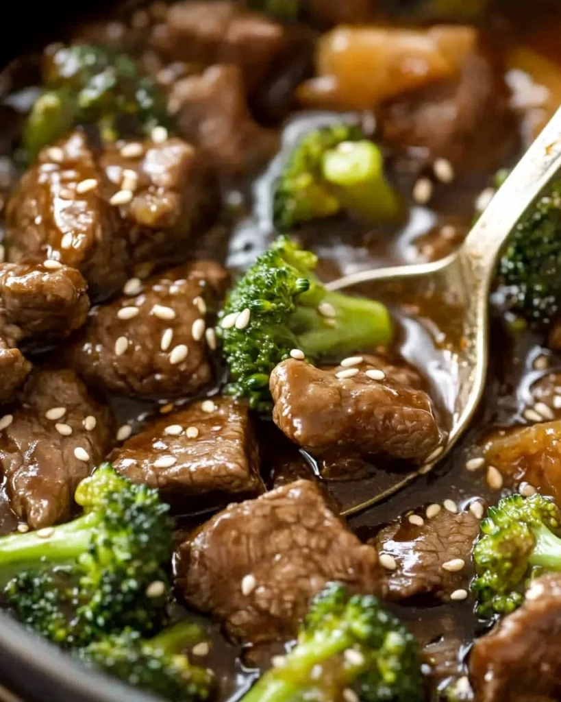 Close-up of beef and broccoli stir-fry topped with sesame seeds and served with a spoon.