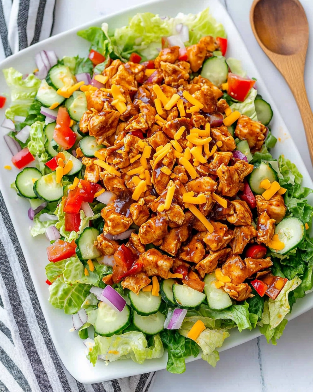 Overhead view of a colorful BBQ chicken salad with fresh vegetables, cheese, and romaine lettuce on a white plate.
