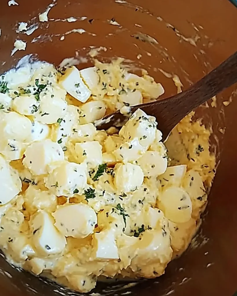 Homemade creamy egg salad with herbs in a mixing bowl and spoon