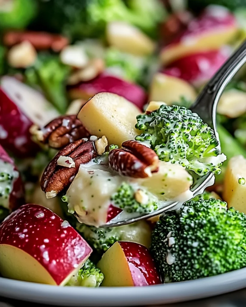Close-up of broccoli apple salad with pecans and creamy dressing on a spoon.