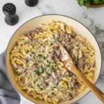 Creamy beef and egg noodle skillet with parsley garnish and white spatula in a rustic pan.