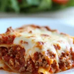 Side view of a cheesy crock pot lasagna slice with meat sauce on a white plate and colorful napkin.