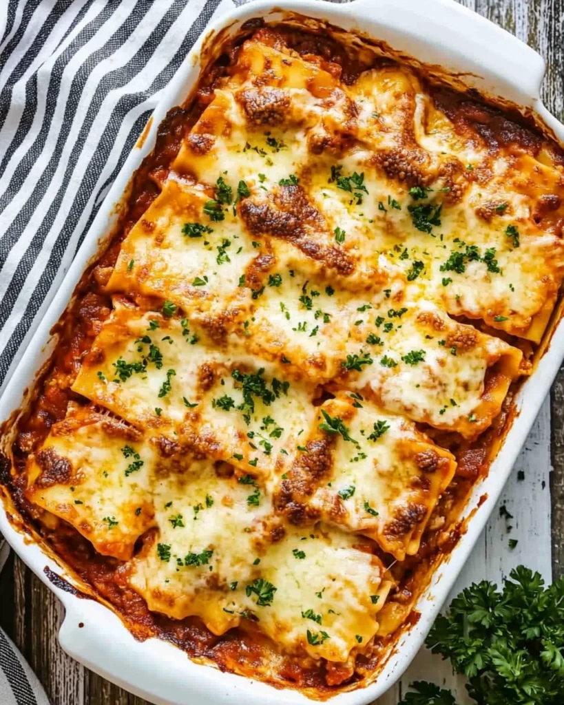 Freshly baked homemade lasagna in a white casserole dish, sliced into squares and topped with golden melted cheese and parsley.