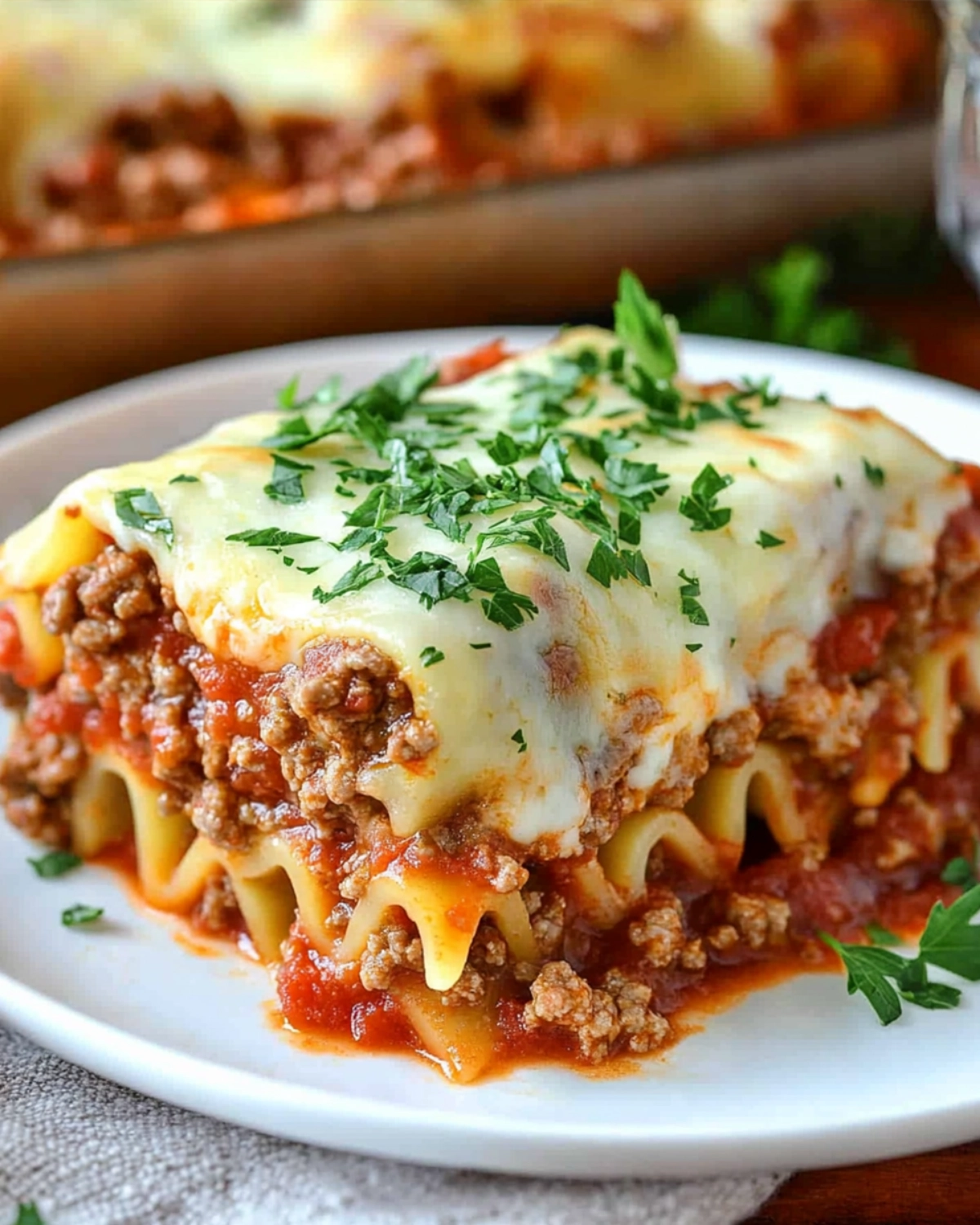 Single serving of cheesy lasagna roll-up on a white plate with ground beef, marinara, and parsley