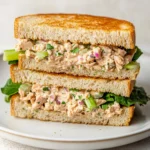 Close-up image of a creamy tuna salad sandwich with lettuce on whole wheat bread, served on a white plate.