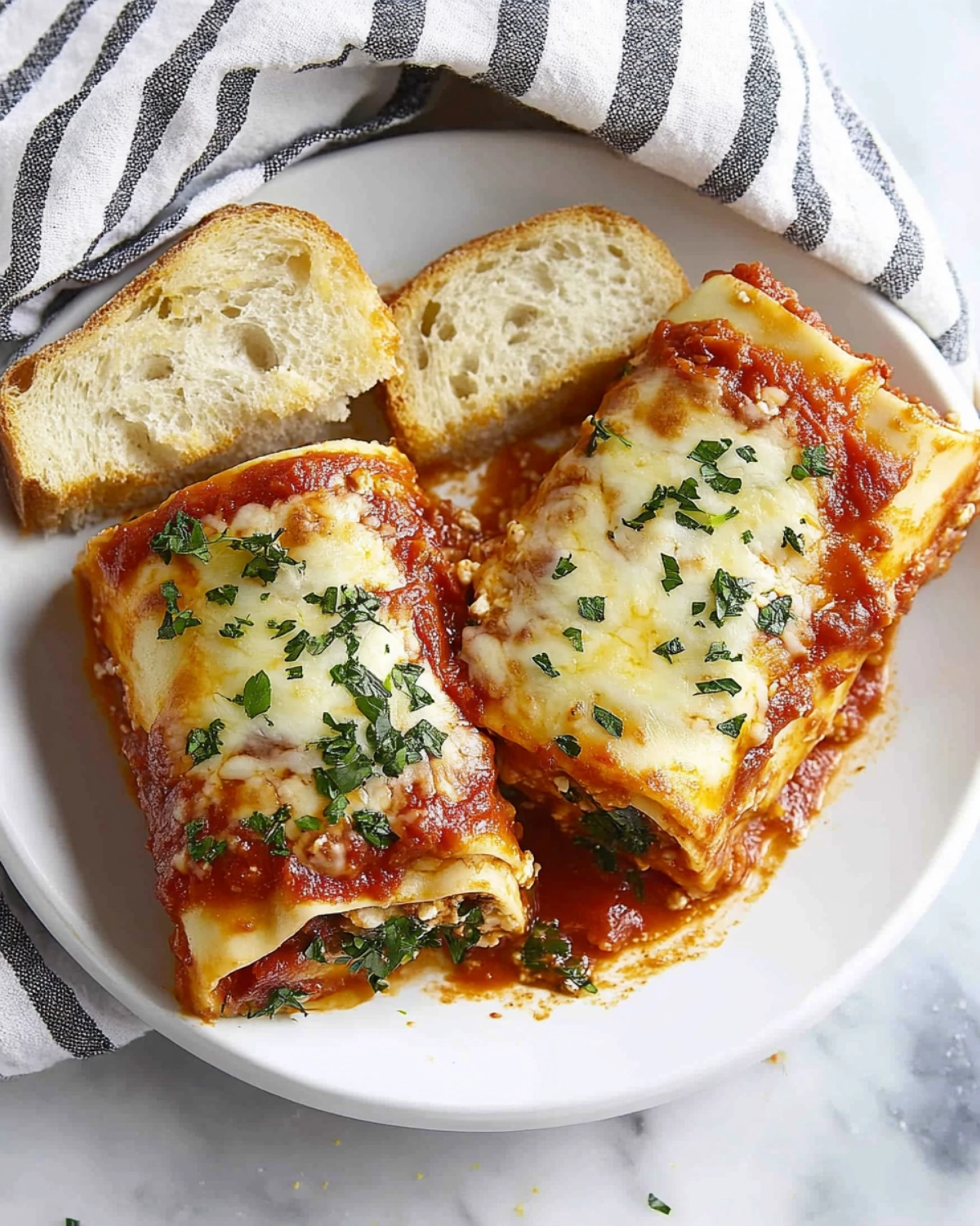 Close-up of cheesy manicotti pasta served with rustic bread on a white plate