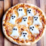 Halloween-themed pizza with cheese ghosts and black olive faces, set on a wooden board.