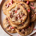Close-up of peppermint chocolate chip cookies topped with crushed candy canes on a white ceramic plate.