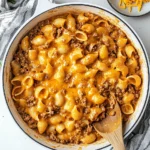 Overhead view of cheesy pasta shells with ground beef in a skillet and serving bowls.