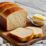 Sliced Amish white bread loaf with butter on a wooden board in a sunlit kitchen