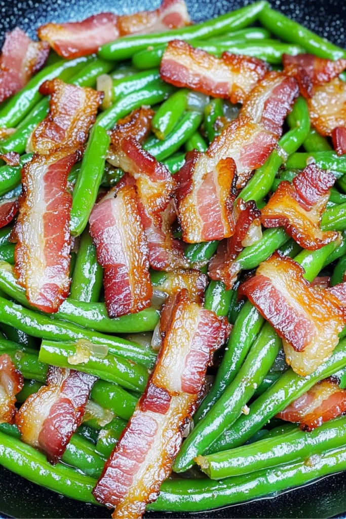 Sautéed green beans with crispy bacon and caramelized onions served on a plate.