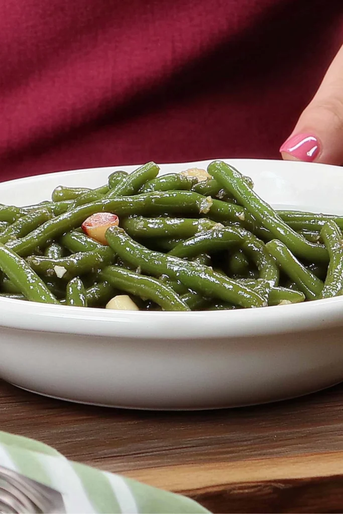 Fresh sautéed green beans with garlic in a white bowl, showcasing their vibrant green color and glossy finish, placed on a wooden surface.