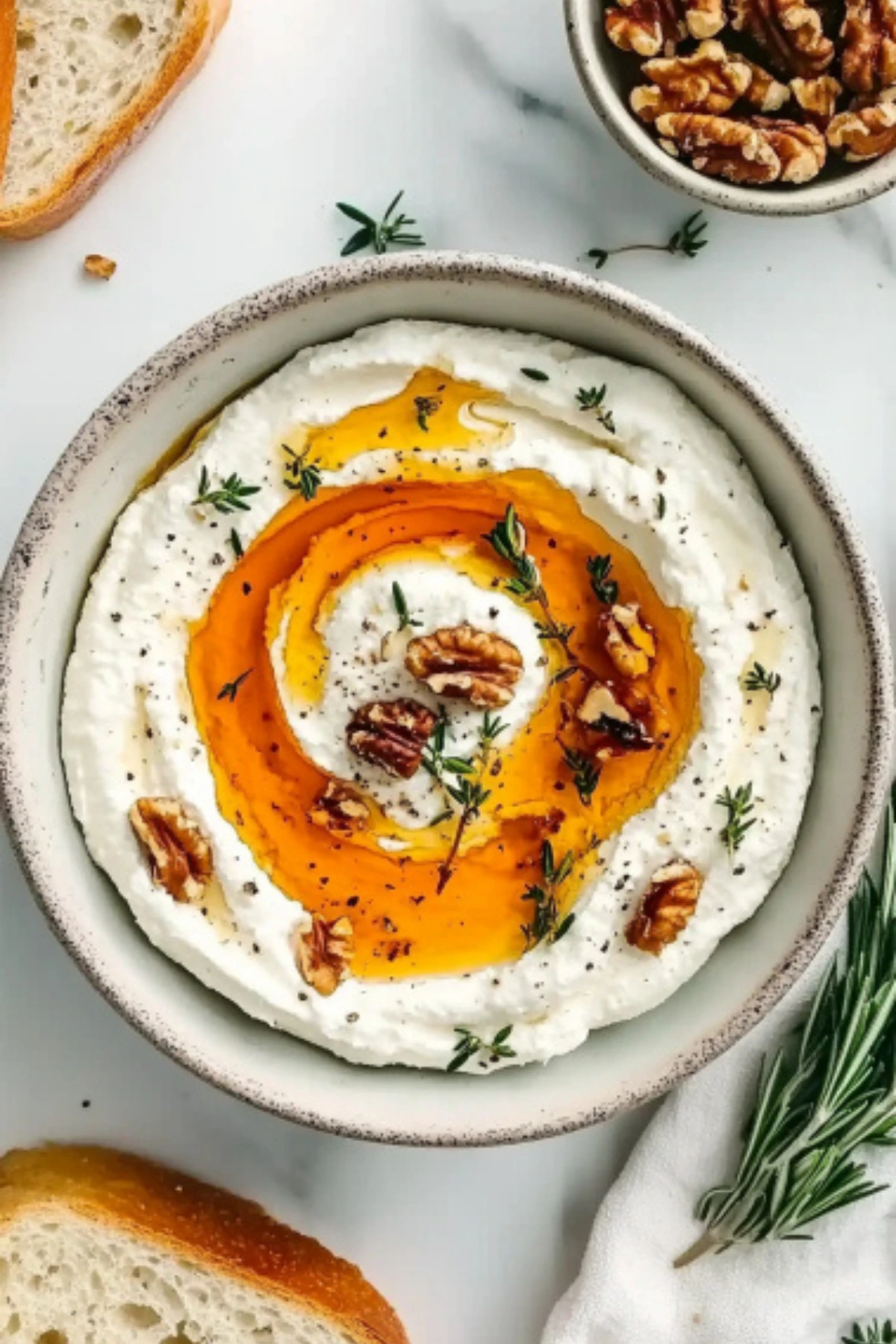 Top view of creamy ricotta dip drizzled with golden hot honey, garnished with walnuts and rosemary