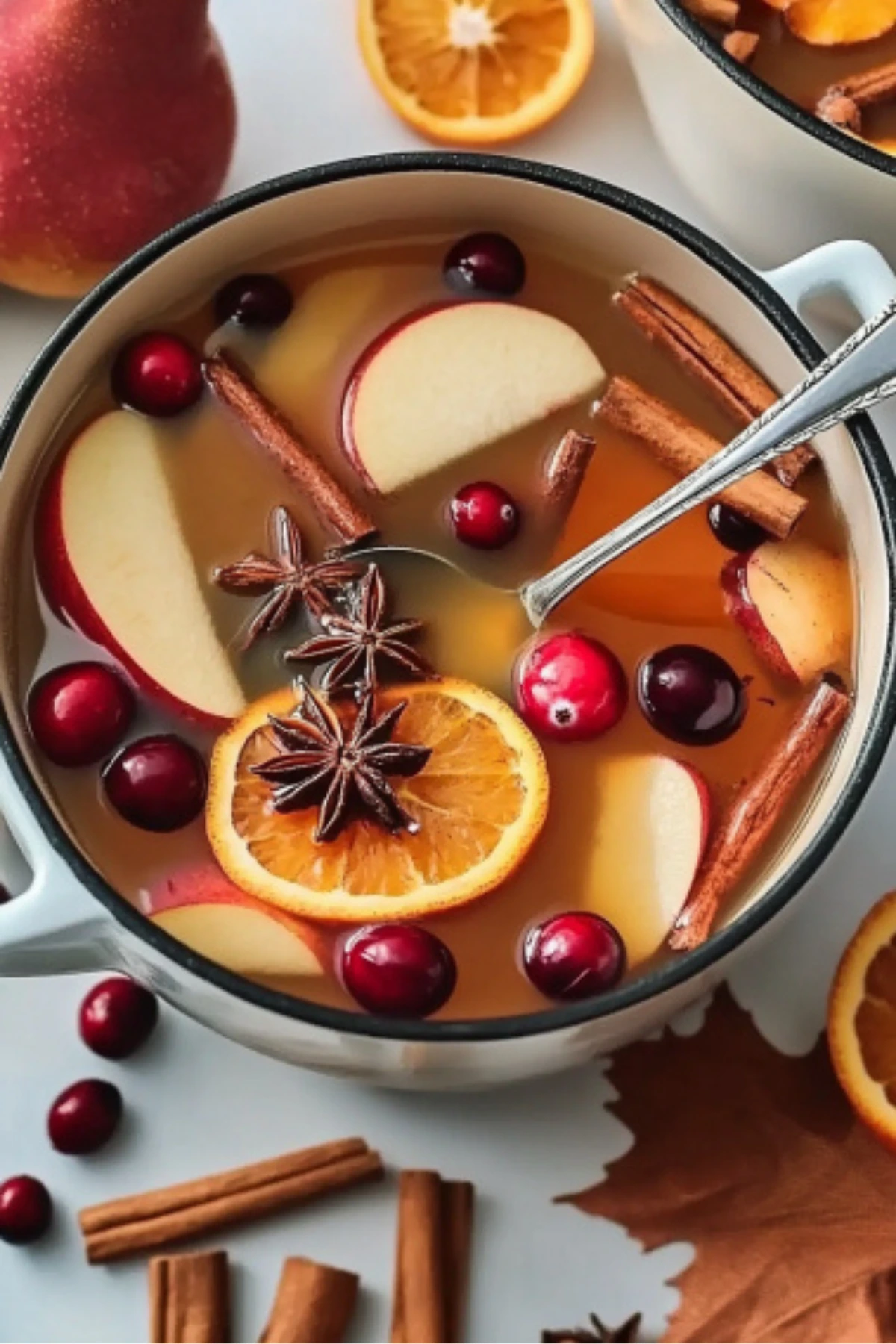 Hot apple cider Thanksgiving punch with orange slices, cranberries, star anise, and cinnamon in a white pot