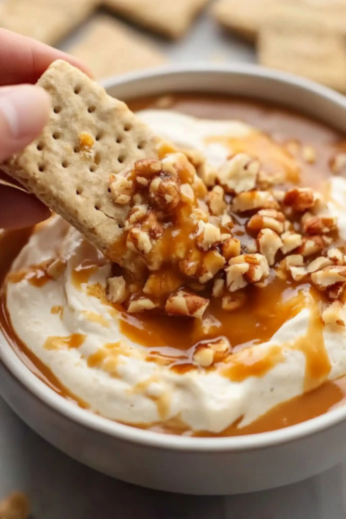 Graham cracker dipped in creamy caramel apple dip topped with chopped pecans and caramel drizzle.