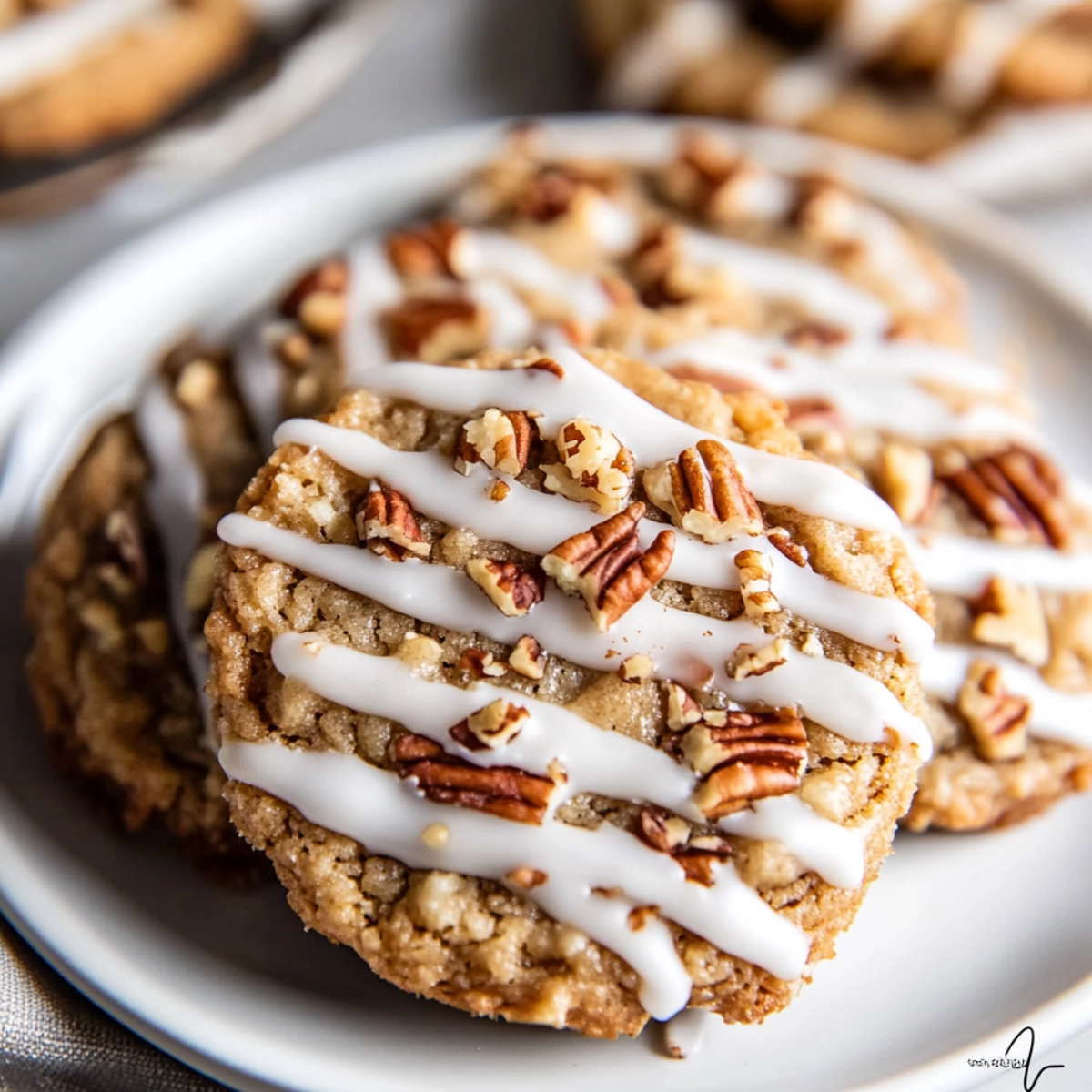 Close-up of glazed pecan cookies with vanilla drizzle on a white plate.