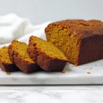 Freshly baked pumpkin bread loaf sliced on a white marble board with a golden brown crust and moist interior.