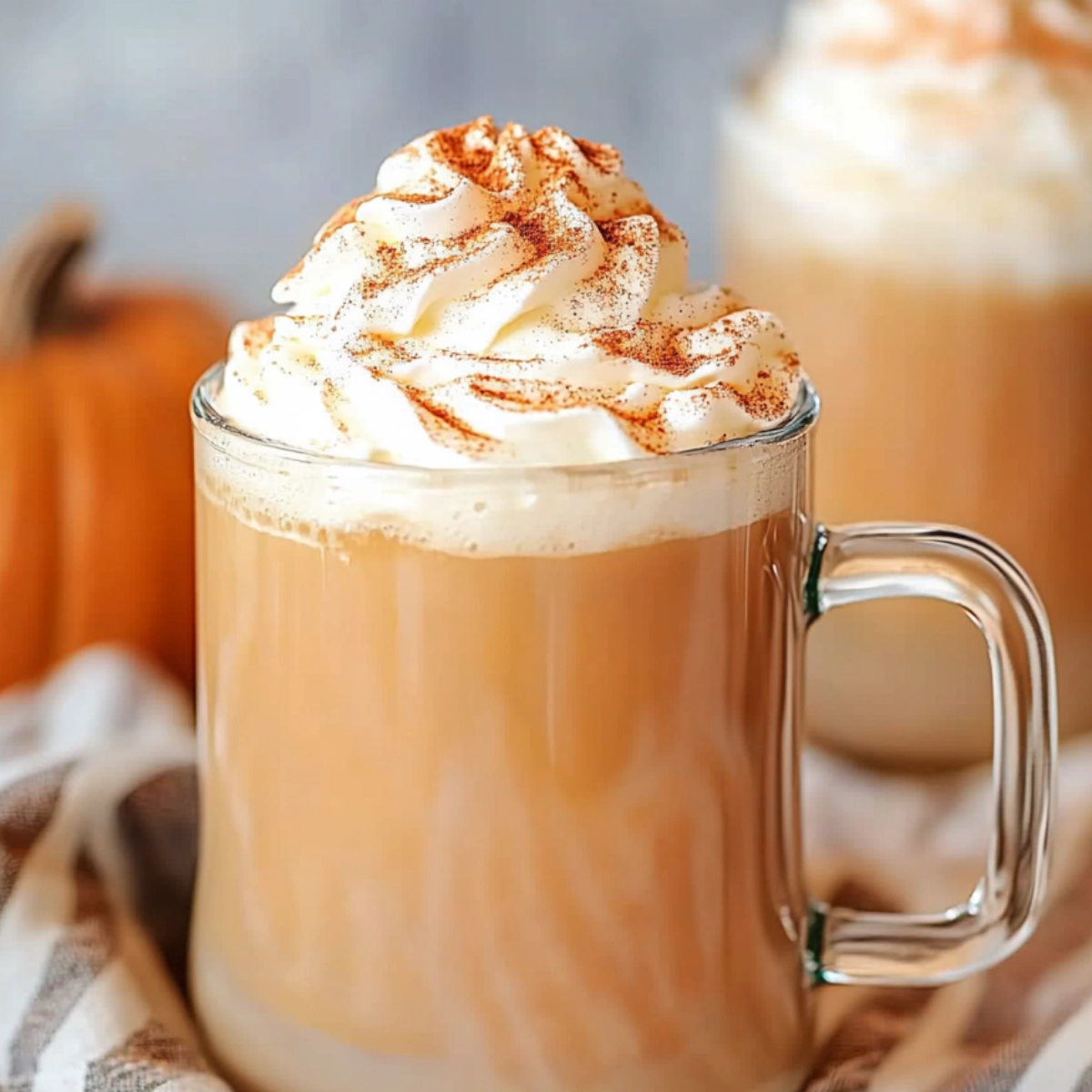 Pumpkin spice latte in a glass mug topped with whipped cream and cinnamon on a cozy autumn background.