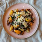 A hearty, homestyle breakfast featuring roasted potatoes, ground beef, sweet peppers, and onions, topped with cheese and fresh herbs, served on a pink plate.