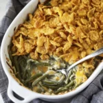 Cheesy green bean casserole topped with crispy fried onions in a white baking dish.