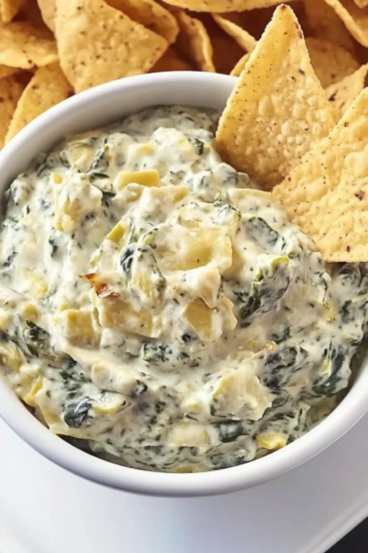 Creamy spinach artichoke dip in a white bowl with tortilla chips