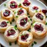 Overhead view of cream cheese cranberry pinwheels garnished with chives and cranberries on a holiday platter