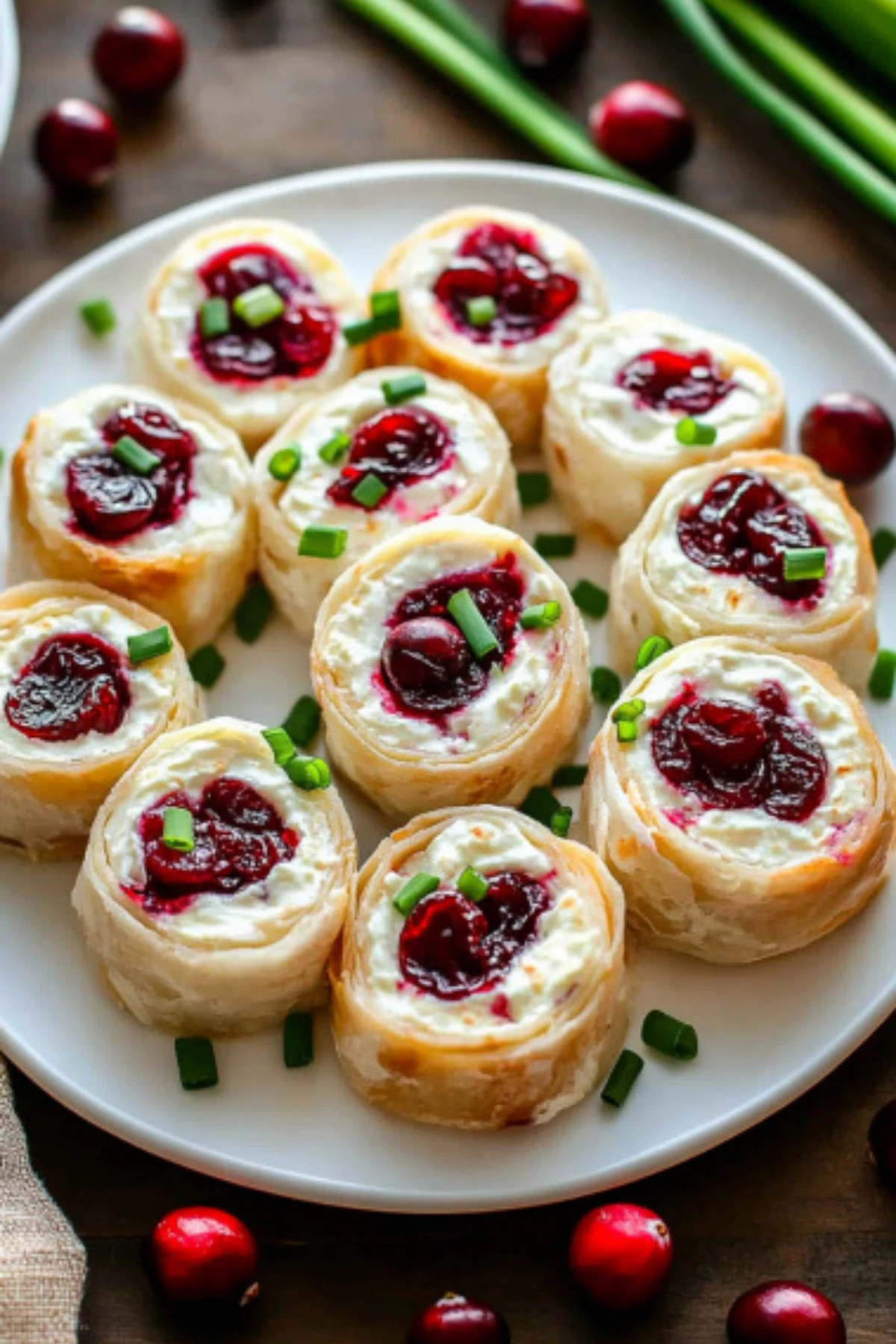 Overhead view of cream cheese cranberry pinwheels garnished with chives and cranberries on a holiday platter