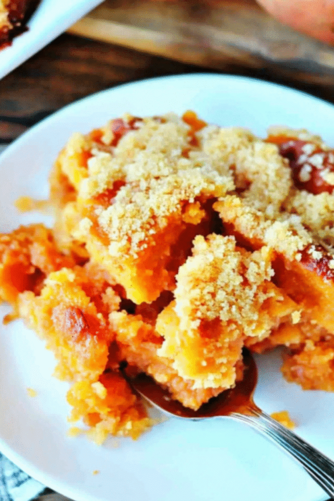 Sweet potato cobbler on a white plate with a spoon, topped with golden brown buttery crumble