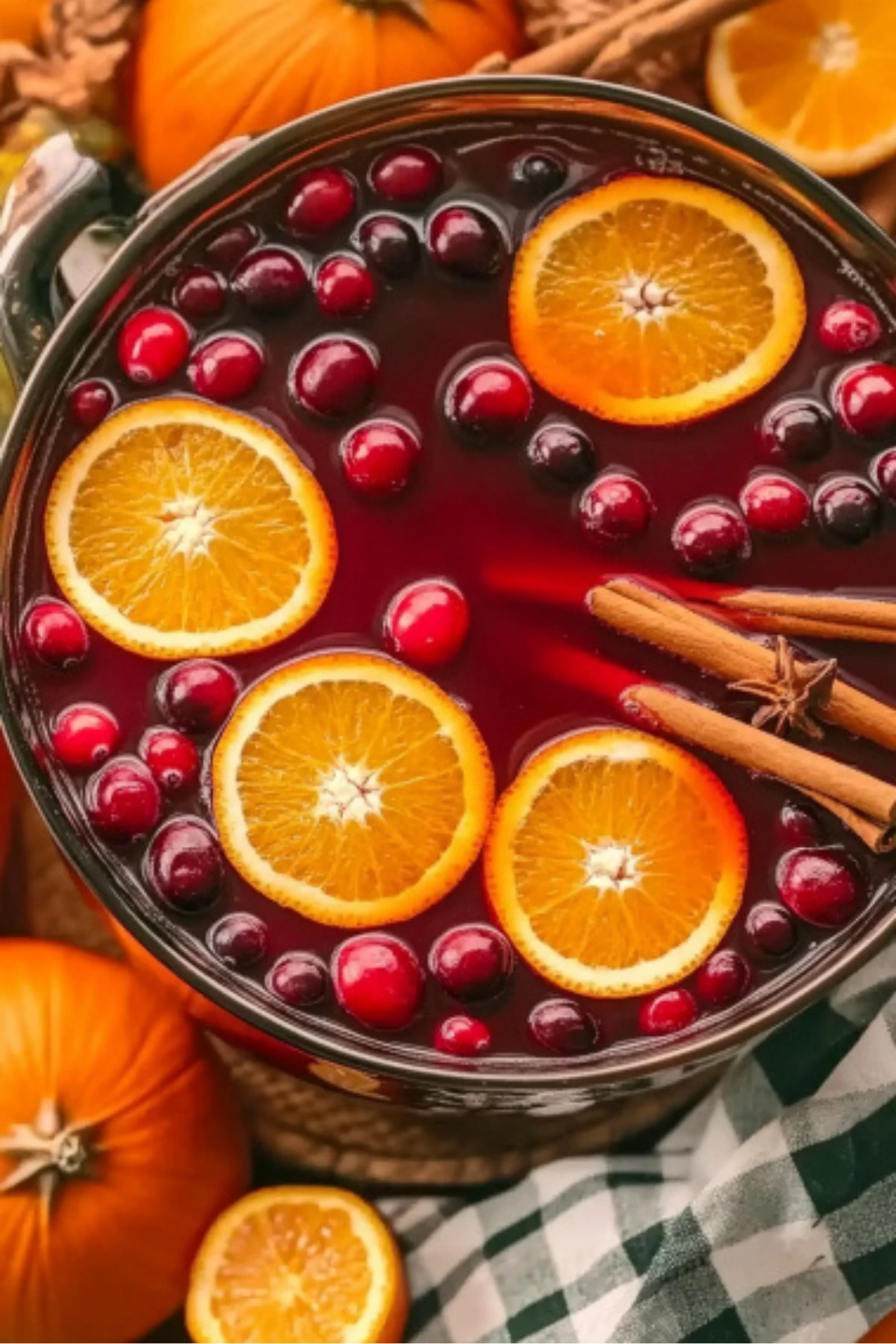 Top view of a festive autumn punch with floating orange slices, cranberries, and cinnamon sticks in a glass punch bowl surrounded by pumpkins