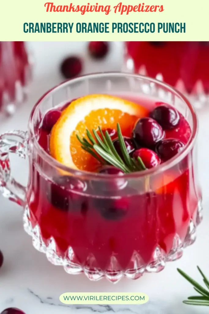 Thanksgiving cranberry orange prosecco punch with orange and rosemary in a glass cup on marble table with holiday garnish