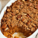 Close-up of freshly baked sweet potato cobbler with pecan streusel topping in a white baking dish.