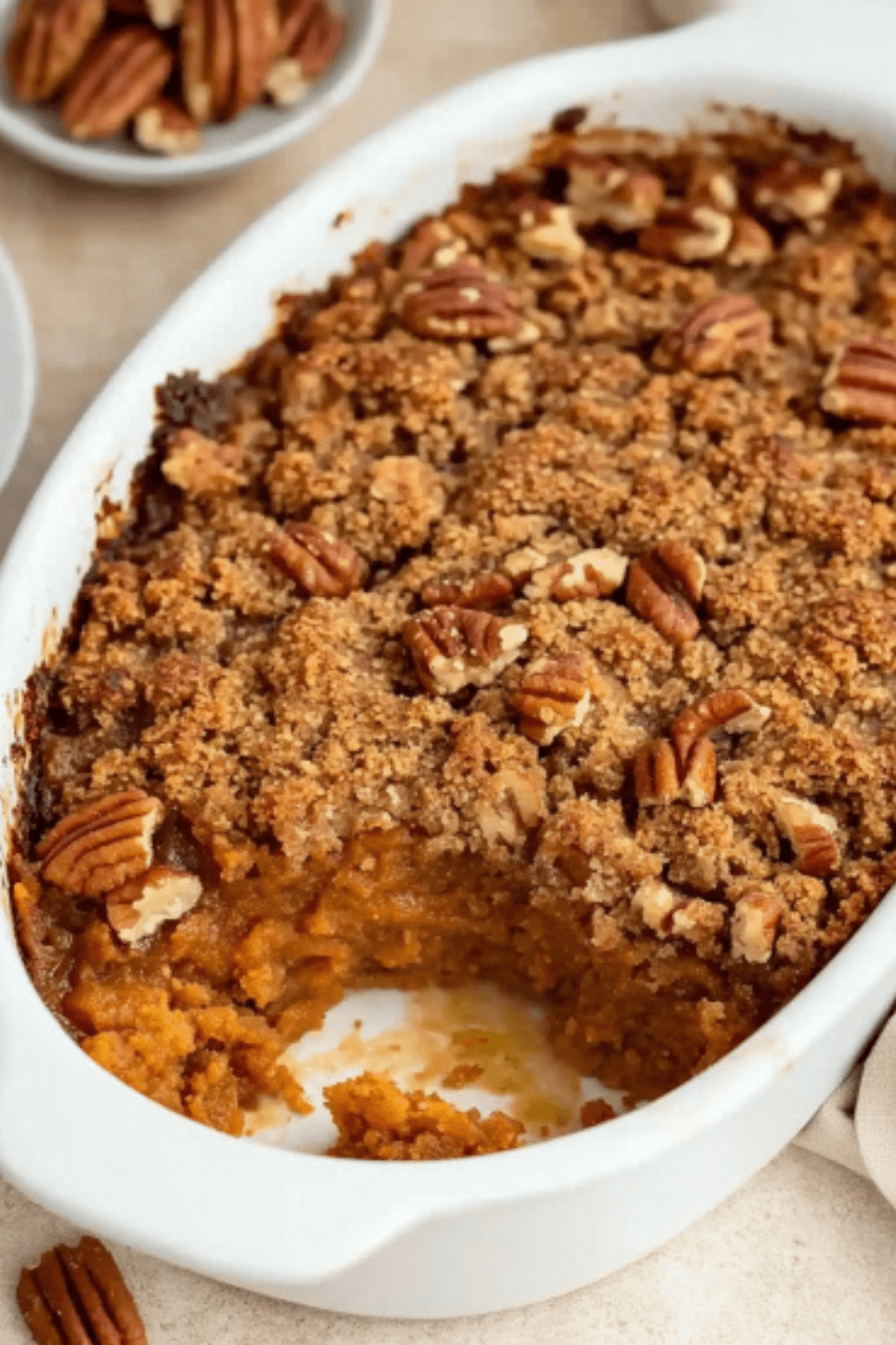 Close-up of freshly baked sweet potato cobbler with pecan streusel topping in a white baking dish.