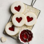 Linzer cookies with heart-shaped centers filled with raspberry jam and dusted with powdered sugar.
